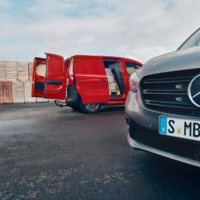 Roter Mercedes-Benz Transporter mit geöffneter Heck- und Seitentür beim Beladen – Nahaufnahme eines zweiten Fahrzeugs im Vordergrund