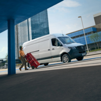 Lieferfahrer mit roten Getränkekisten vor weißem Mercedes-Benz eSprinter – geparkt im Ladebereich vor Bürogebäuden
