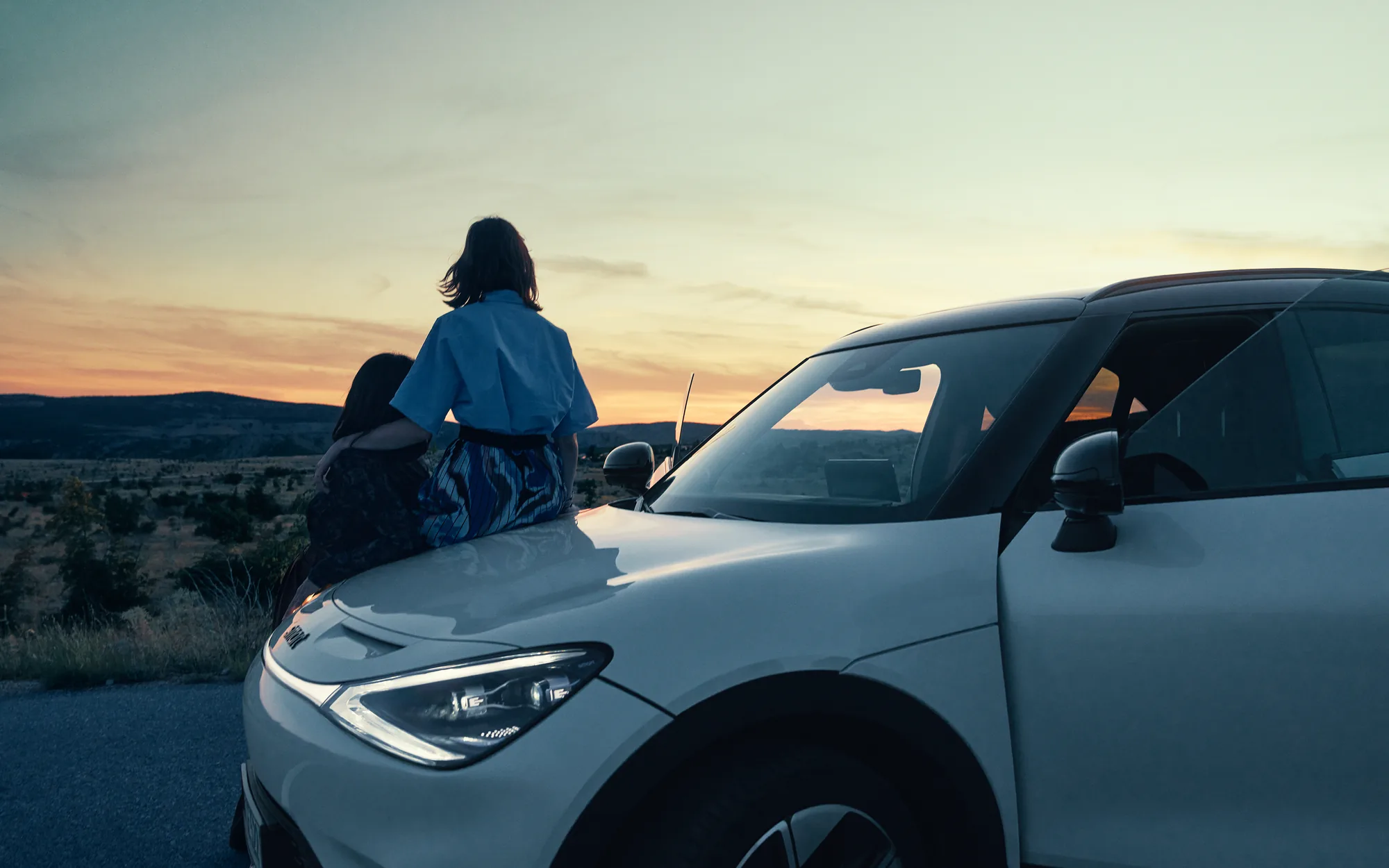 Zwei Frauen sitzen bei Sonnenuntergang auf der Motorhaube eines weißen smart #3