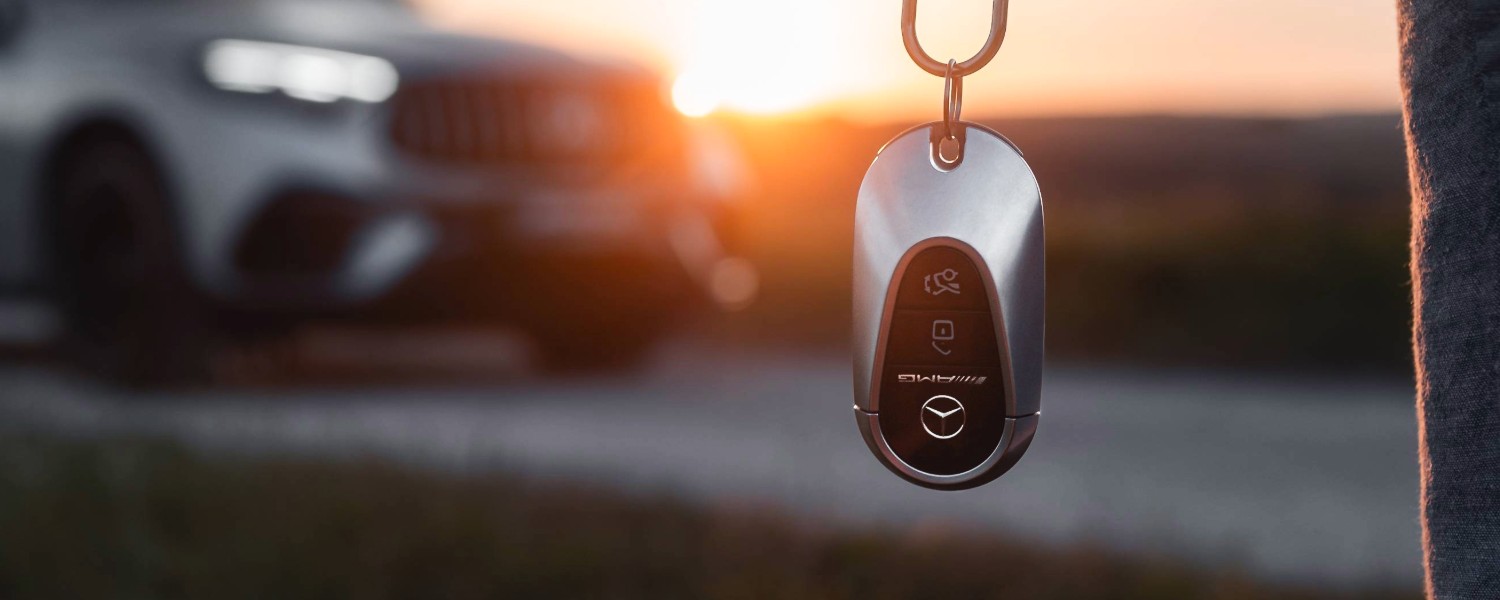 AMG Autoschlüssel im Vordergrund, unscharf im Hintergrund ein Mercedes-Benz GLC AMG auf einem Feldweg im Schwarzwald bei Sonnenuntergang.